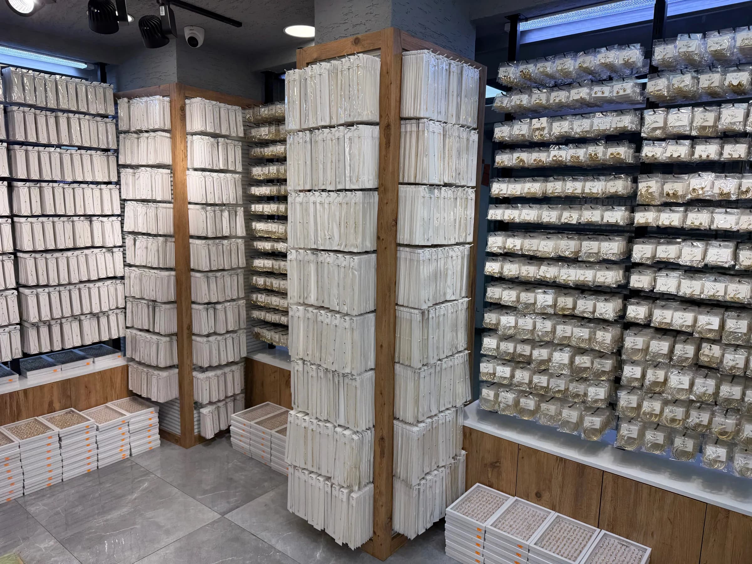 Bijuteri mağazasında ahşap çerçeveli askılı teşhir kolonları; arkada kanallı pano duvarda poşetli küpeler