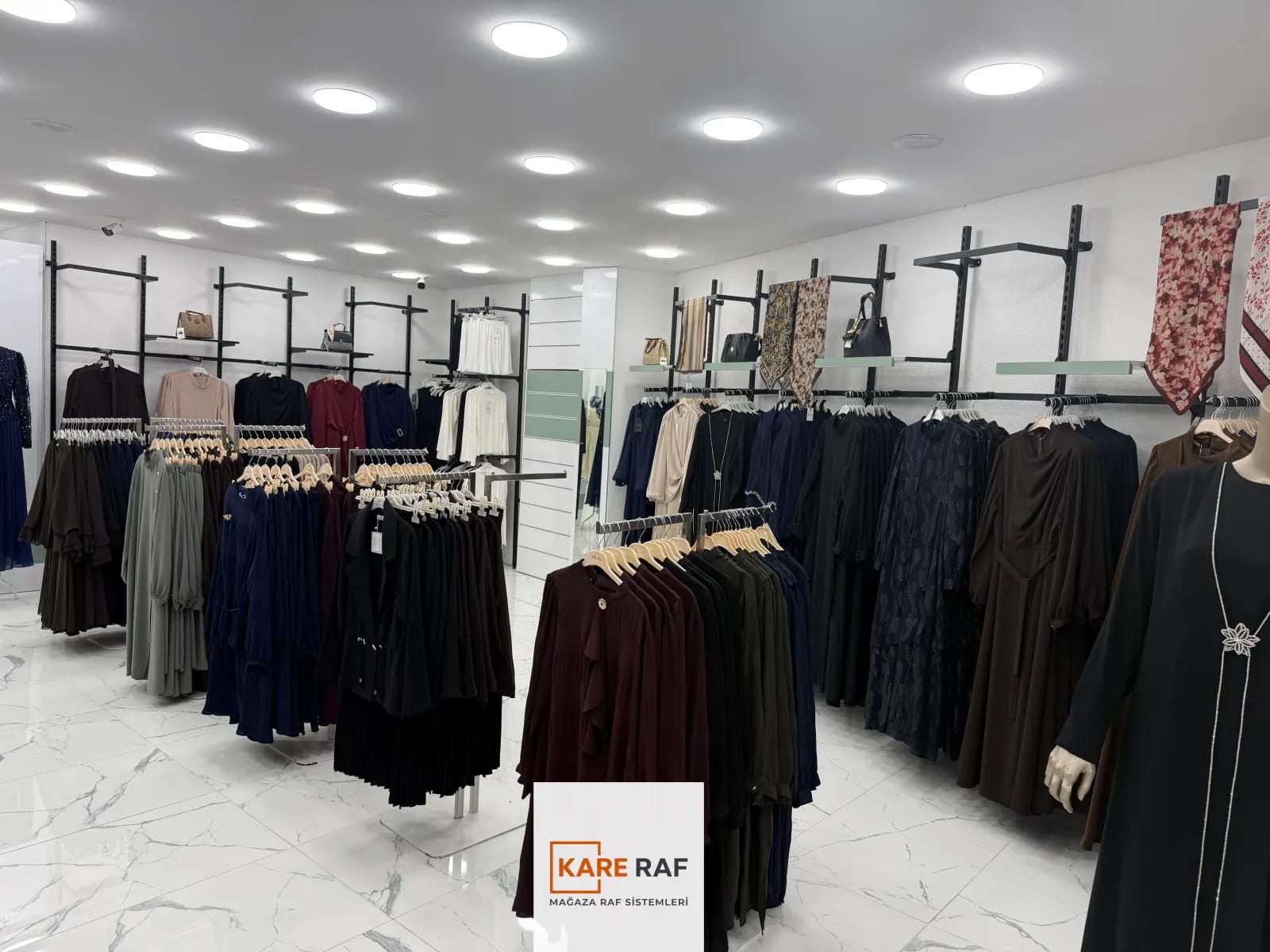 Armira mağazasında raflı siyah dikmeli duvar askıları, koyu renk ferace ve abiyeler, önde manken